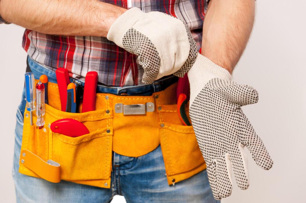 getting ready to work close up of handyman with tool belt wearing protective gloves while standing against grey background photo